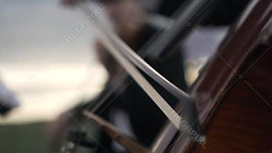 Caucasian cellist plays bow on cello on background blurred violinist at sunset