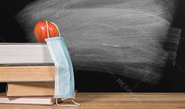 Back to virtual school background concept with stack of books and apple with face mask