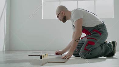 Bald handyman in workwear uses level to check parquet floor