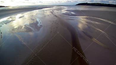 Hovering over a stream on a large beach at dusk to the seashore. Nobody, cloudy weather. 4K UHD aerial shot, low altitude.