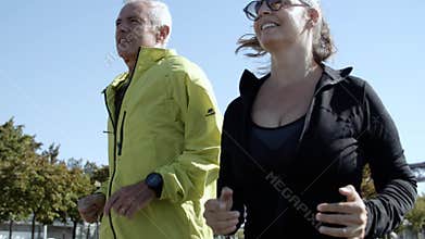 Couple of happy older runners jogging down street