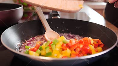 Woman hands adding colorful pepper cubes mix to frying pan