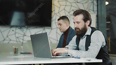 An image of two programmers working on a laptop and a tablet. Web programmers at remote work. Man's gaze at the camera.
