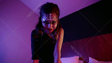 Sexy lady with artistic makeup is posing passionately and flirting with camera, sitting in bedroom at night