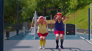Senior man woman doing active training stretching muscles squatting fitness exercising on playground
