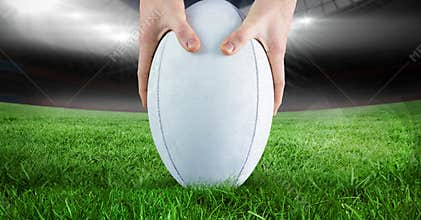 Close up of hands placing a rugby ball on grass field against stadium