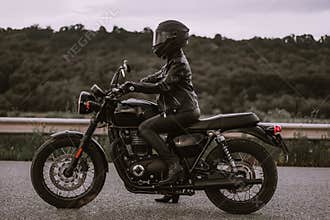 Portrait of confident motorcyclist woman in motorcycle helmet. Young driver biker looking away outdoors alone on highway