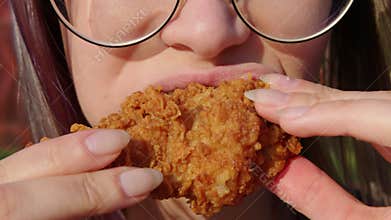 Young woman with glasses eating fried chicken