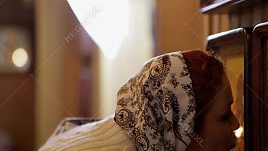 A young woman in a headscarf prays in an Orthodox church and puts candles in front of icons