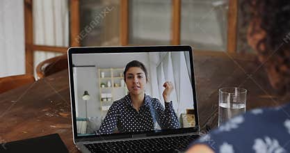 Businesswomen talking through videoconference, laptop monitor view over woman shoulder