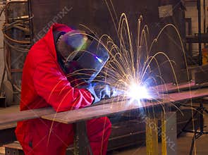 Welder bends to cut metal beam with orange sparks.