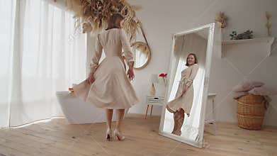 Happy charming female in new dress spinning around in front mirror indoors