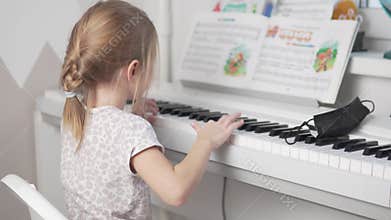 Little girl playing the electronic piano on the children's notes at home, the view from the back