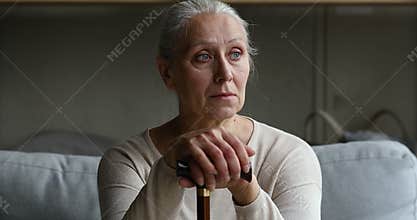 Sad old lady sit on couch lean on walking cane