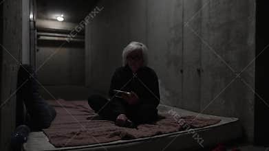 Woman is sitting on a mattress in a bomb-shelter during russian invasion in Ukraine