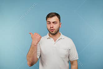 Handsome man in white t-shirt standing on blue background with serious face and pointing fingers aside at copy space