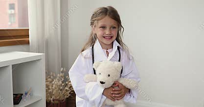 Little girl in white coat holding fluffy toy pose indoor