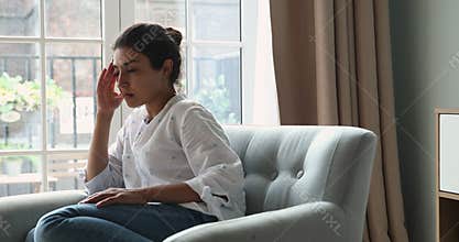 Worried Indian woman sit on armchair looks concerned, feels depressed