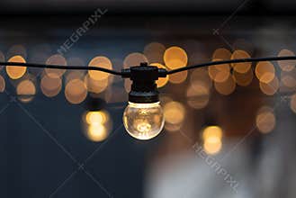 Electric lamp garlands with different size bulbs hanging in a cafe, attached to the ceiling. Evening party or wedding decorations