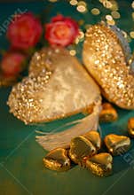 Heart shaped chocolates in golden foil on an old table. Dark blurred background with bokeh. Flowers. Wedding greeting