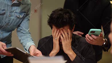 Close-up face of exhausted shocked businessman sitting at office desk, male and female colleagues shaking papers over