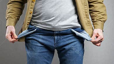Poor man looks for money in jeans pockets on grey background