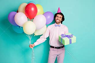 Portrait of smiling guy hold colorful balloons present box dressed formalwear cone isolated on turquoise color