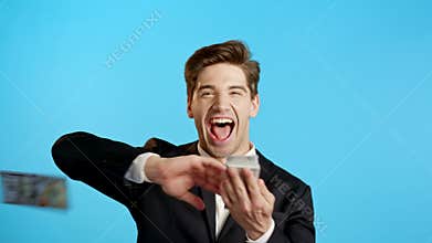 Business man with happy face scatters money. People overspend US currency. Guy is flush with dollars on blue studio