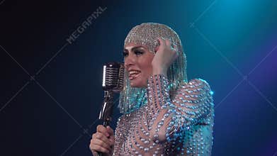 A charming woman in a chic shiny headdress and costume in rhinestones dances and sings into a vintage microphone against