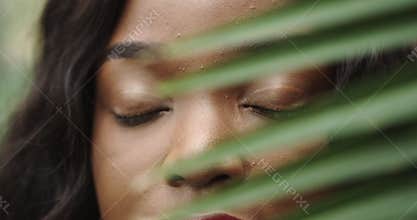 Beautiful girl African American with tanned skin poses and walks among tropical plants. Natural makeup and wet hair in a