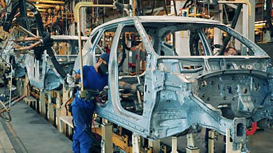 Several car factory workers using a welding machine on a car assembly line. Automobile factory interior. Industrial