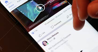 Details with the hand of a man browsing through the Facebook app on a mobile device.