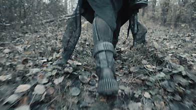 Close-up following shot of female legs stepping. Woman in futuristic military clothes feet walk along path in dead