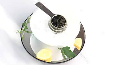 Glass jar with black caviar on ice with lemon, parsley