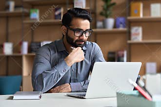 Serious indian business man working or studying on laptop computer.