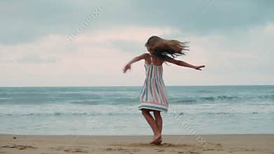 Happy girl spending vacation at seashore. Young woman dancing at coastline.