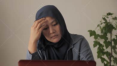 Asian muslim woman thinking contemplation while working on her laptop, sad emotion expression