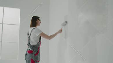 Brunette builder paints wall near window with mini roller