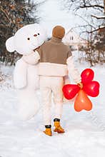 Young man from behind hugs holding big teddy bear soft toy gift heart air balloons on this special day surprising girlfriend. roma