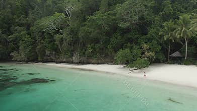 Beautiful Girl Walking On Ocean Beach With Huts Among Palm Trees In Triton Bay, Raja Ampat. Stunning View From Drone