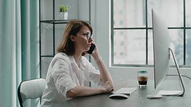 Lady boss makes call near computer sitting at table in room
