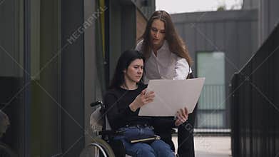 Disabled Caucasian CEO in wheelchair discussing business project with assistant outdoors. Serious successful women