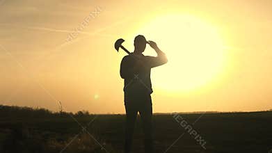 A farmer walks through the field with a shovel in rubber boots to dig the soil of the land at sunset, agriculture, land