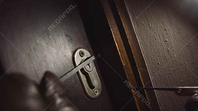 Intruder or Burglar with lock pick tool opens the front door to enter the house