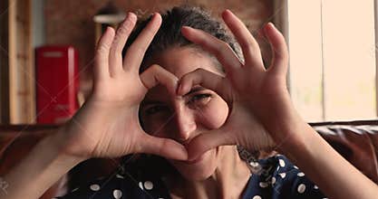 Happy young woman showing heart symbol to camera.