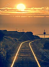 Railroad train tracks leading to ocean at sunset