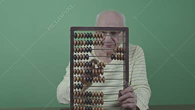 Mature man using abacus while sitting at table viewed through frame of abacus