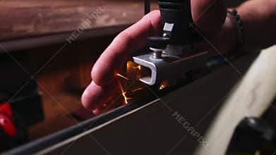 Close-up. Male hands sharpening the edge of a snowboard in a ski rental shop. Low key. Shallow depth of field.