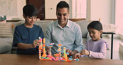 Focused Indian dad and kids constructing city from toy blocks