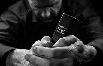 A Man praying holding a Bible.